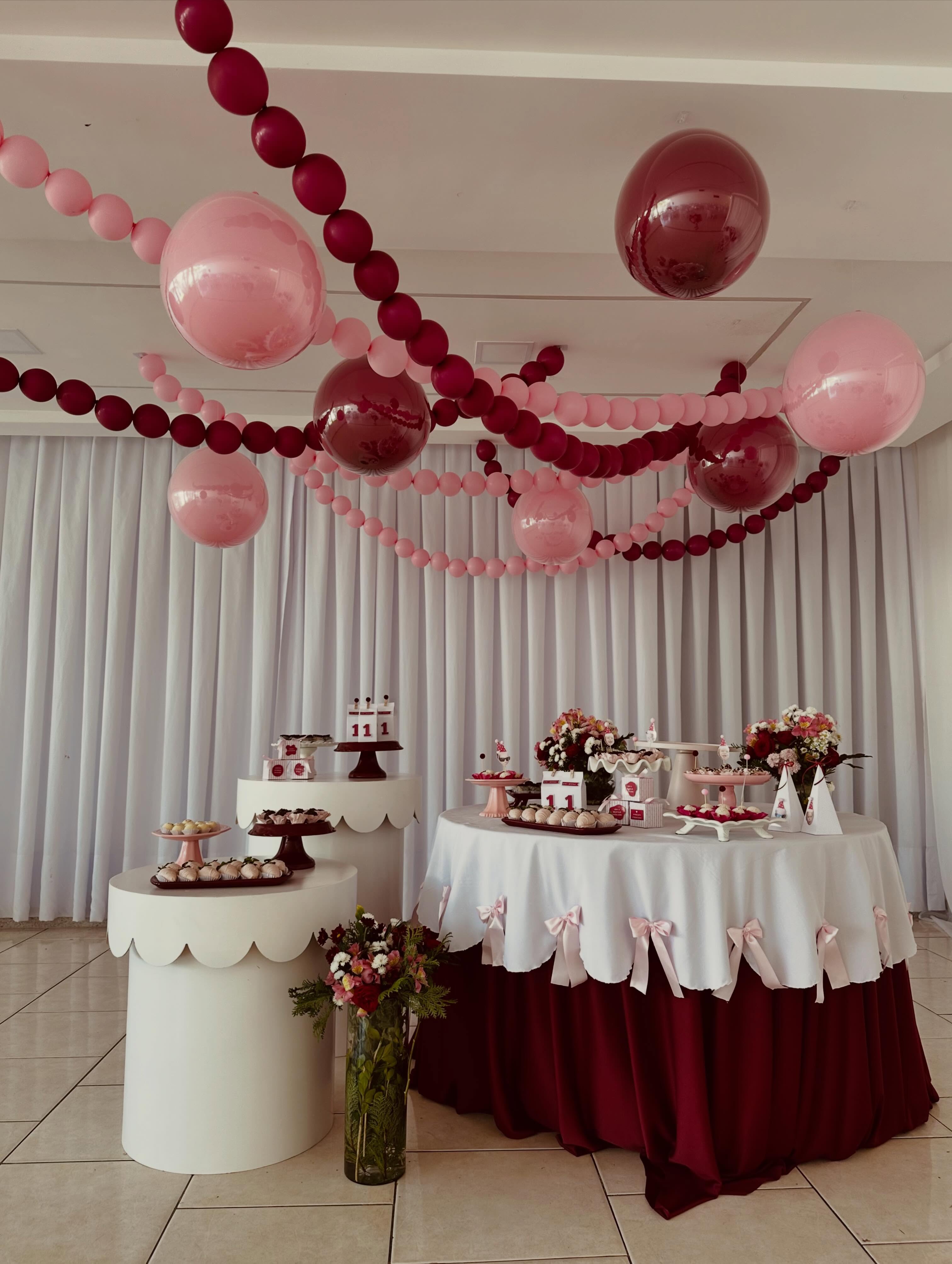 Correntes de balões rosas e vinho atravessam o teto, com balões encapsulados sobre a mesa de uma festa de aniversário.