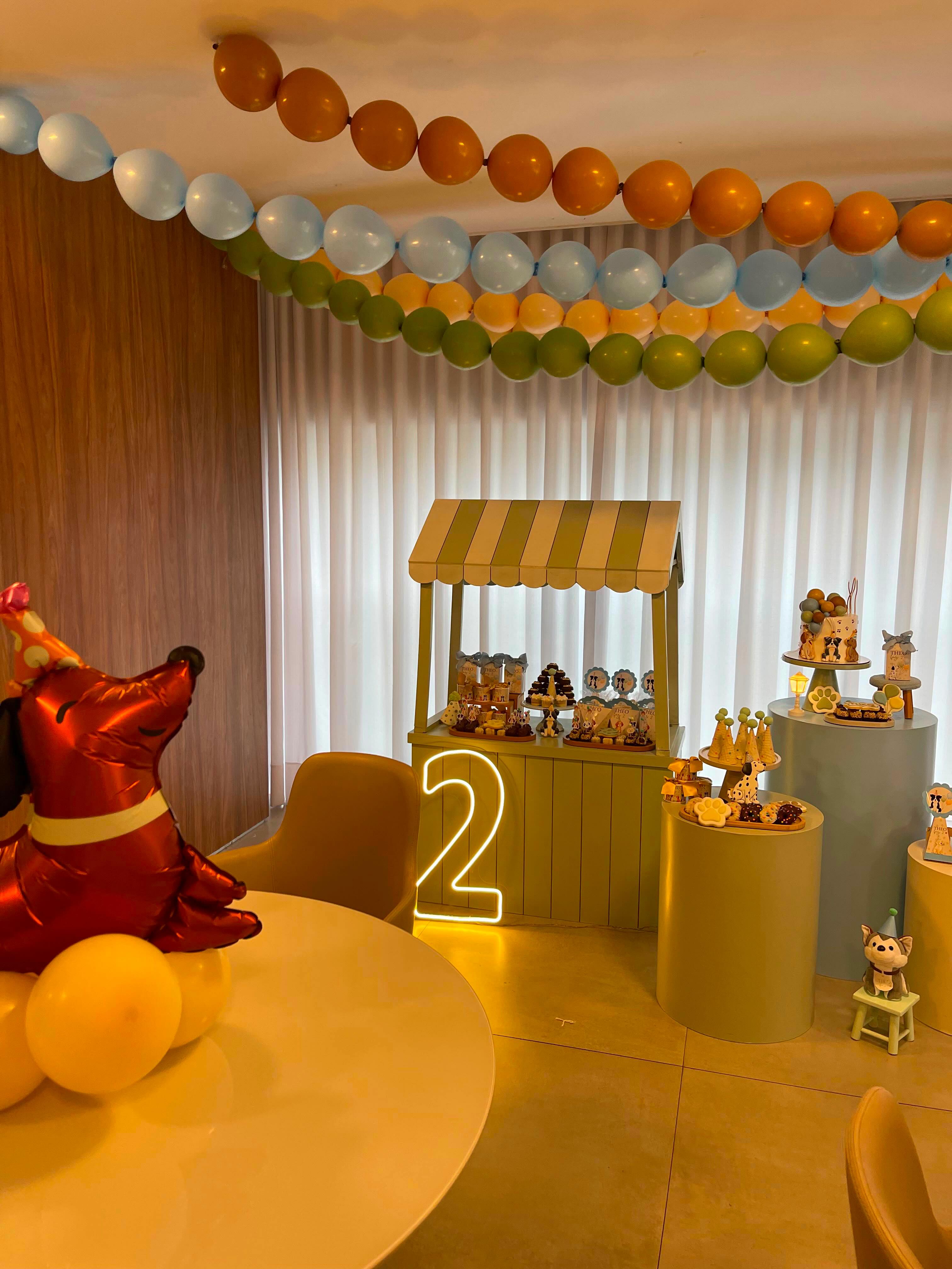 Decoração de aniversário infantil com balões em tons suaves, uma pequena quitanda temática e detalhes de cachorrinhos.
